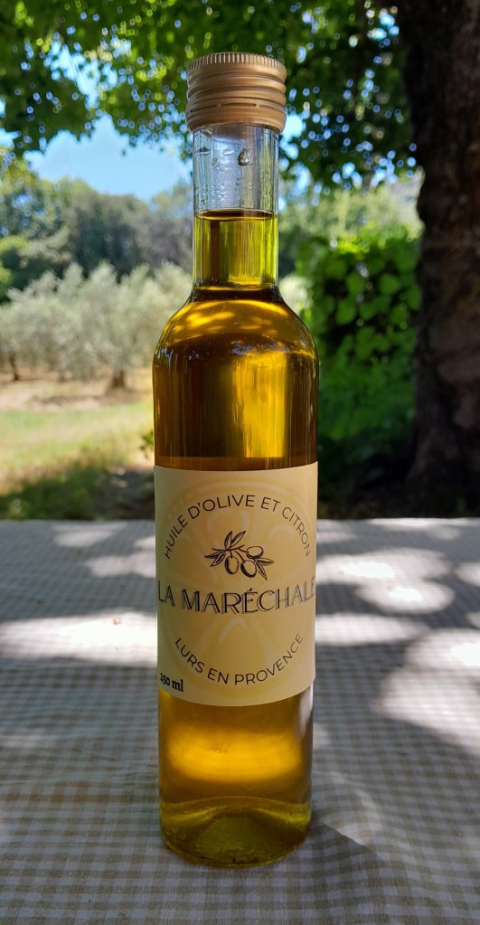 Bouteille en verre contenant de l'huile, sur fonds de vergers d'oliviers. L'étiquette indique : "Huile d'olive et citron La Maréchale Lurs en  Provence"